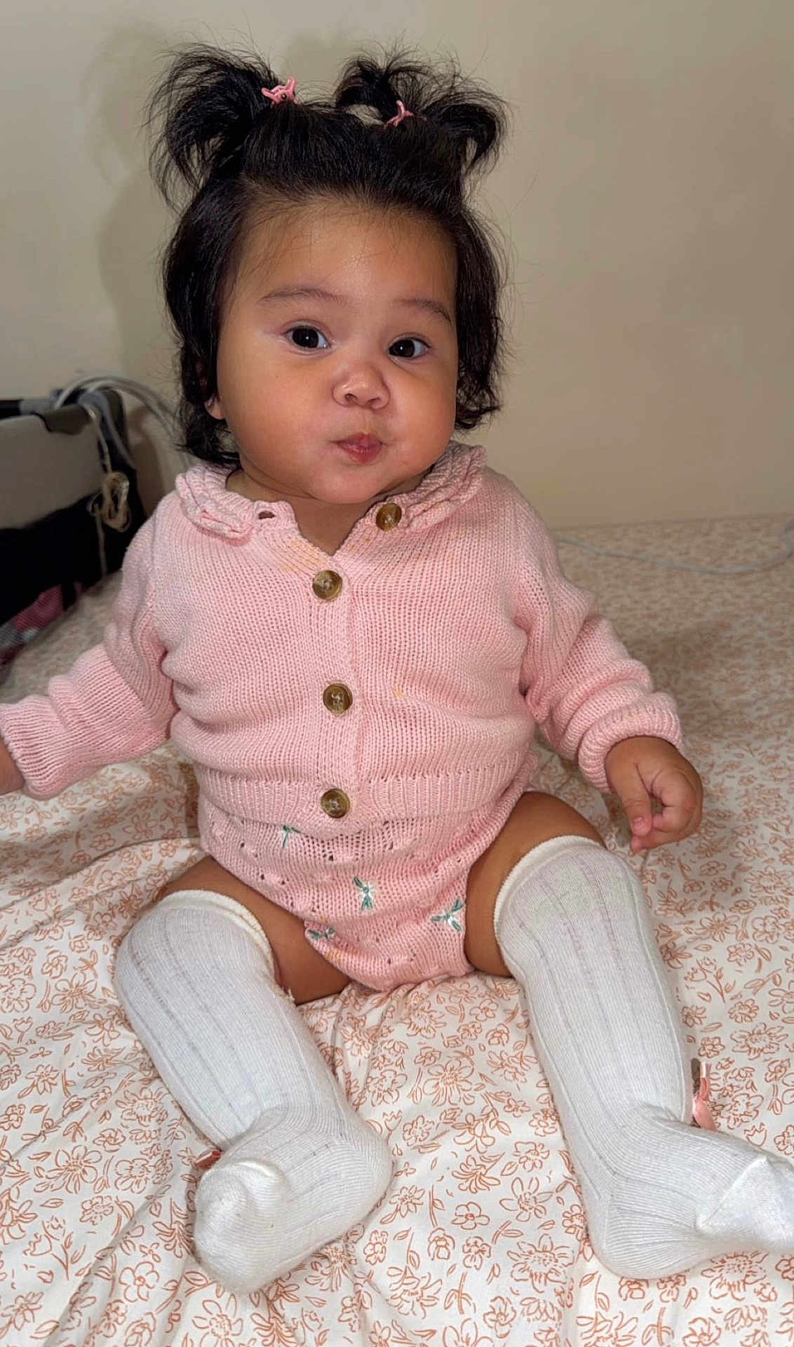 Kataleya is registered to the contest to win money with this photo: baby, infant, toddler, portrait, sitting, pink_sweater, knitted, buttons, knee_socks, white_socks, floral_bedding, bedroom, hair_clips, pigtails, chubby_cheeks, cute_expression, indoor, cozy, child, adorable
