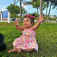 Liyana is registered to the contest to win money with this photo: toddler, child, grass, outdoor, park, palm_trees, pink_dress, bows, happy, smiling, summer, nature, greenery, sunny, baby, sitting, cute, playful, daytime, casual_clothing