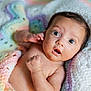 baby, infant, newborn, blanket, crochet_blanket, pastel_colors, surprised_expression, wide_eyes, portrait, closeup, skin, hand, lying_down, cute, cozy, soft_texture, nursery, bokeh, photography, face