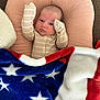 baby, infant, blanket, stars, stripes, pillow, cushion, face, person, indoors, carpet, sleepwear, newborn, cute, resting, soft_texture, cozy, portrait, young_child, comfort
