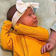 Honey is registered to the contest to win money with this photo: baby, infant, headband, bow, yellow_clothing, ribbed_fabric, blanket, lying_down, side_view, hand, soft_texture, cute, child, newborn, portrait, skin, small_hand, indoors, cozy, baby_girl