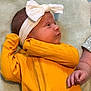 baby, infant, headband, bow, yellow_clothing, ribbed_fabric, blanket, lying_down, side_view, hand, soft_texture, cute, child, newborn, portrait, skin, small_hand, indoors, cozy, baby_girl
