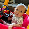 baby, child, toy_car, steering_wheel, pacifier, indoor, couch, cushion, red, yellow, playful, smiling, clothing, short_sleeve, person, infant, seat, hand, foot, portrait
