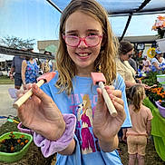 Sydney Guest is registered to the contest to win money with this photo: child, girl, glasses, butterfly, stick, netting, outdoor, market, flowers, plants, people, blue_shirt, purple_scrunchie, smile, nature, daylight, event, casual_clothing, hair, portrait