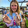 child, girl, glasses, butterfly, stick, netting, outdoor, market, flowers, plants, people, blue_shirt, purple_scrunchie, smile, nature, daylight, event, casual_clothing, hair, portrait