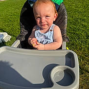 Asher joined the competition — help win amazing prizes! toddler, high_chair, outdoor, grass, sunlight, child, snack, seat, parked_cars, red_hair, baby_clothing, summer, playful, sunny_day, person, food, hand, expression, greenery, daylight