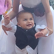 David joined the competition — help win amazing prizes! baby, child, girl, toddler, dress, tuxedo, smiling, outdoor, person, family, holding, happy, celebration, footwear, white_dress, vest, young, cute, supporting, socks