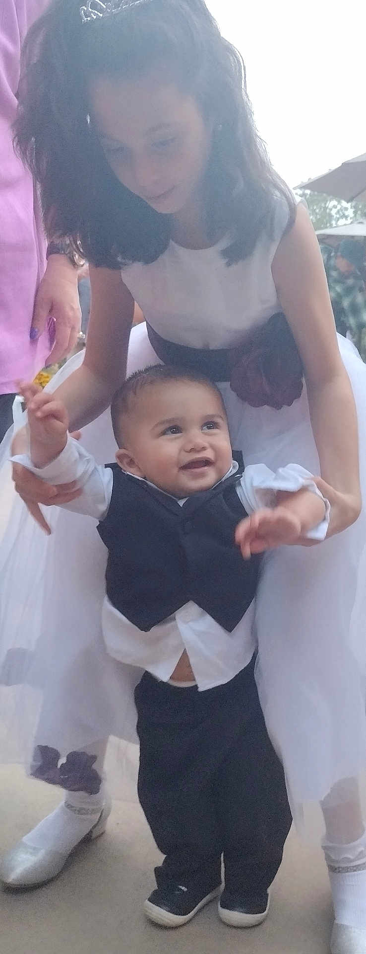 David joined the competition — help win amazing prizes! baby, child, girl, toddler, dress, tuxedo, smiling, outdoor, person, family, holding, happy, celebration, footwear, white_dress, vest, young, cute, supporting, socks