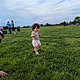 child, toddler, grass, outdoor, park, people, sky, clouds, greenery, walking, summer, casual_clothing, curly_hair, nature, daylight, recreation, family, fun, leisure, field
