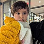 toddler, child, person, face, clothing, jacket, yellow, white, indoor, holding, portrait, curious, soft_lighting, blurred_background, baby, young_child, cute, warm_clothing, hand, people