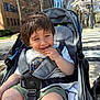 toddler, child, stroller, outdoor, sunlight, urban, trees, building, spring, baby, happy, smiling, clothing, seatbelt, playful, shorts, white_shirt, daytime, sidewalk, nature