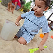 Baha participe au concours pour gagner de l'argent avec cette photo : child, boy, sand, shovel, bucket, playground, outdoor, playing, summer, casual_clothing, shorts, tshirt, toy, kneeling, daylight, nature, tree, blurred_background, person, fun