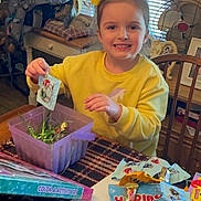 Aurora joined the competition — help win amazing prizes! child, girl, yellow_sweatshirt, smile, candy, table, chair, window, blinds, container, packet, indoor, home, decorations, wooden_table, paper_towel, color_activity_set, happy, person, toy