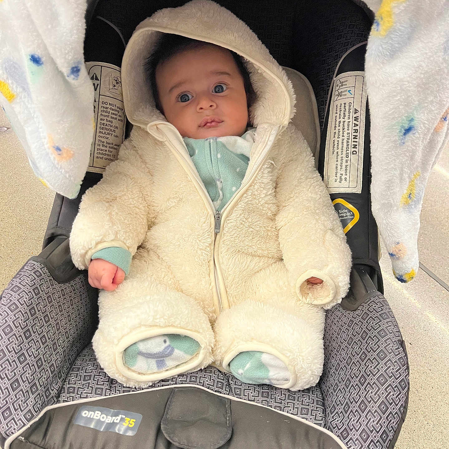 Evan is registered to the contest to win money with this photo: baby, blanket, blue_eyes, bundle, car_seat, child, clothing, comfort, cute, fabric, face, hood, indoor, infant, onesie, patterned, portrait, seated, warm_clothing, young_child