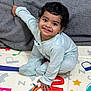 toddler, child, smiling, pajamas, play_mat, colorful, indoor, blanket, happy, curly_hair, baby, floor, hand, face, sitting, cute, infant, home, person, young_child