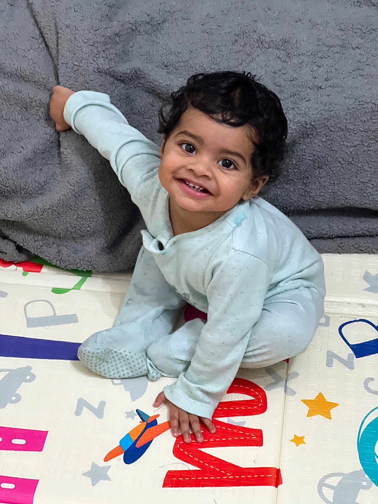 Alric joined the competition — help win amazing prizes! toddler, child, smiling, pajamas, play_mat, colorful, indoor, blanket, happy, curly_hair, baby, floor, hand, face, sitting, cute, infant, home, person, young_child