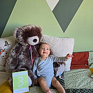 Charlie participe au concours pour gagner de l'argent avec cette photo : baby, teddy_bear, bed, pillow, blanket, milestone_card, wall_art, child, infant, smiling, indoor, soft_toy, clothing, furniture, person, cute, happy, sitting, portrait, home
