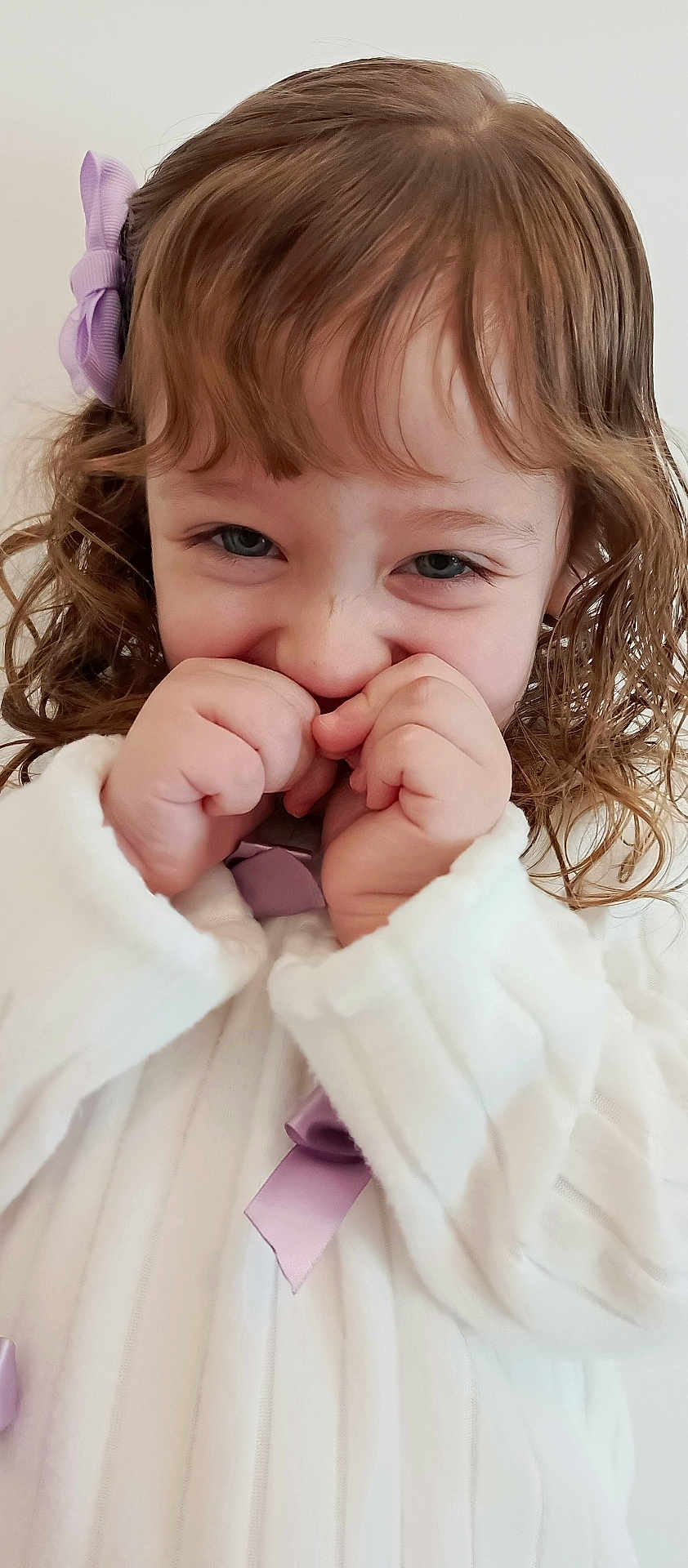 Maitê participe au concours pour gagner de l'argent avec cette photo : child, toddler, girl, curly_hair, hair_bow, white_dress, hands, fingers, close_up, portrait, smile, playful, blue_eyes, face, bangs, cute, indoor, skin, ribbon, gesture
