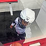 child, helmet, hockey, sports, glass, barrier, hand, fist, hoodie, mickey_mouse, indoors, bench, floor, white, red, black, person, protective_gear, young, action