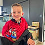 Matheo participe au concours pour gagner de l'argent avec cette photo : child, boy, smile, red_sweatshirt, super_mario, indoor, kitchen, modern, recycling_bin, black_jacket, happy, casual, seated, short_hair, person, light_skin, furniture, window, wood_floor, face