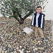 Matheo a rejoint le concours — aidez-le/la à gagner de superbes lots ! child, boy, tree, rocks, pebbles, outdoor, smiling, casual_clothing, jacket, sneakers, nature, daylight, wall, ground, portrait, standing, young, greenery, leaves, background