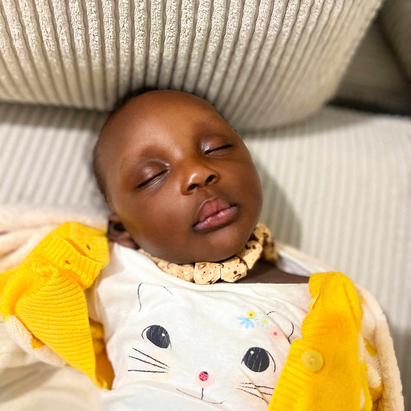 Isis a rejoint le concours — aidez-le/la à gagner de superbes lots ! baby, sleeping, child, face, onesie, cat_print, yellow_cardigan, necklace, couch, texture, closeup, peaceful, indoors, soft_lighting, portrait, resting, cozy, infant, cute, relaxation