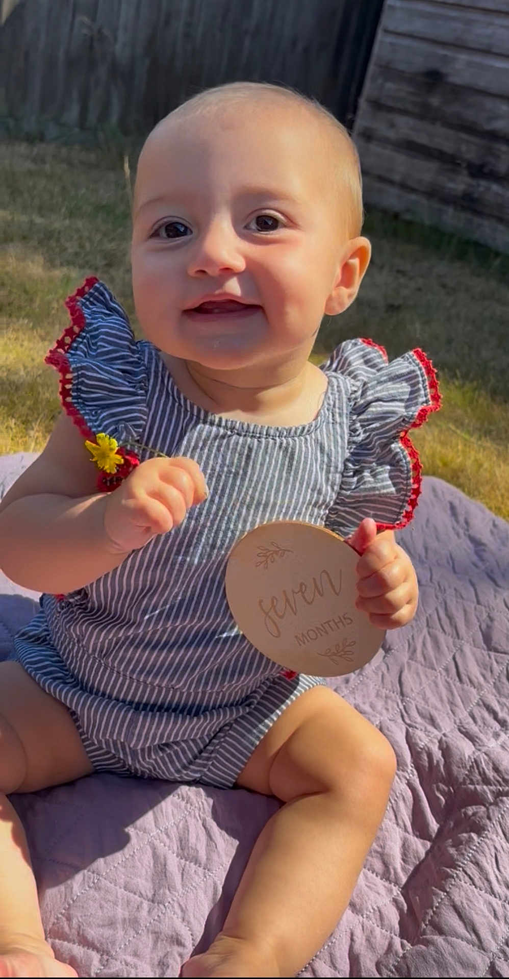 Analeigh joined the competition — help win amazing prizes! baby, child, infant, outdoor, sunlight, quilt, flower, wooden_sign, striped_clothing, smiling, sitting, cute, summer, nature, portrait, grass, fence, happy, person, hands