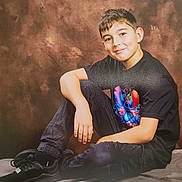 Kelyan participe au concours pour gagner de l'argent avec cette photo : child, boy, smile, casual_clothing, black_shoes, black_pants, tshirt, indoor, studio, portrait, sitting, bench, young, short_hair, colorful_graphic, relaxed, background, pose, happy, photography