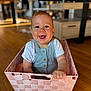 baby, child, smiling, basket, woven_basket, indoor, wooden_floor, happy, person, white_shirt, blue_overall, cute, infant, home, furniture, living_room, portrait, sitting, hand, playful