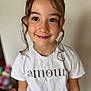 amour, blurry_background, brown_eyes, casual_clothing, child, curly_hair, cute, face, fashion, girl, happy, indoor, necklace, person, portrait, smile, tendrils, text, white_shirt, young