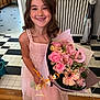 Ashley a rejoint le concours — aidez-le/la à gagner de superbes lots ! child, girl, smiling, dress, pink, flower_bouquet, indoor, barefoot, radiator, wooden_floor, tile_floor, happy, long_hair, necklace, decor, home, person, holding, portrait, cute