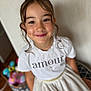 amour, blurred_background, brown_eyes, casual_clothing, child, colorful_toys, curly_hair, cute, face, furniture, girl, happy, home, indoor, necklace, portrait, skirt, smiling, toy_basket, white_shirt