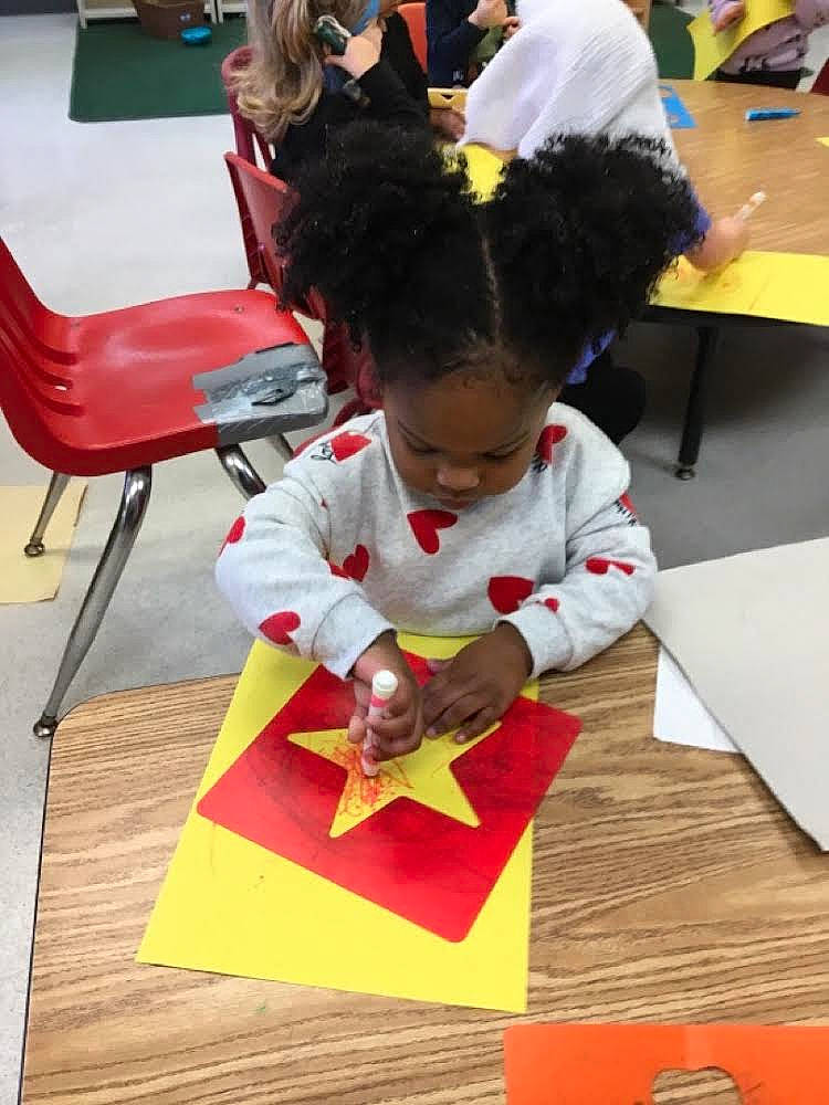 Queen is registered to the contest to win money with this photo: carmine, chair, child, education, event, flooring, fun, kindergarten, learning, leisure, person, play, reading, recreation, room, sharing, sitting, table, toddler, wood