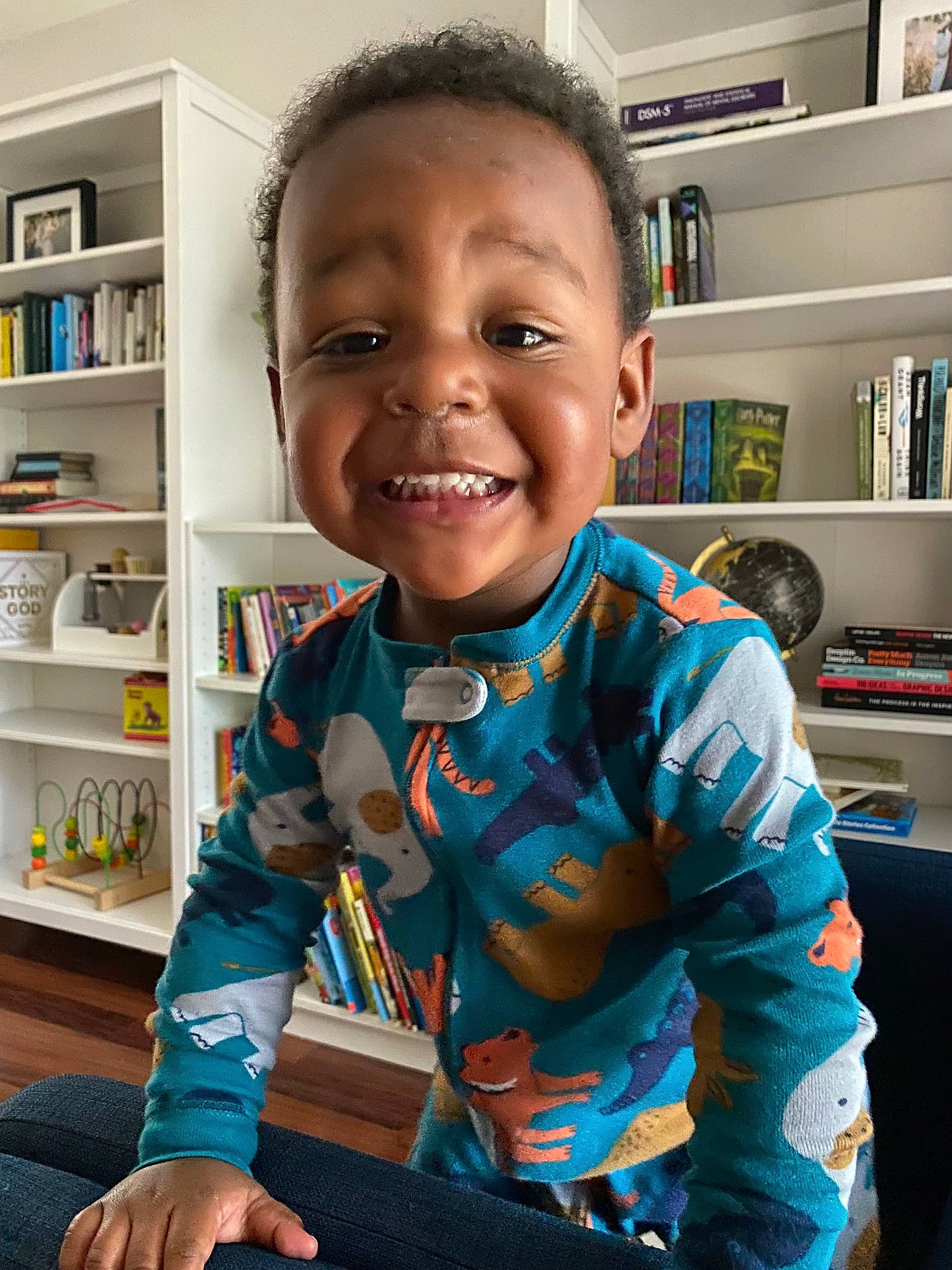 Aiden is registered to the contest to win money with this photo: bookcase, cheek, child, electric_blue, facial_expression, finger, fun, happy, iris, joy, person, play, room, shelf, shelving, sitting, skin, sleeve, smile, t_shirt