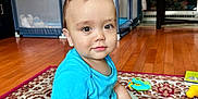 Zachary is registered to the contest to win money with this photo: toddler, child, toy, plush_toy, carpet, wooden_floor, blue_shirt, green_pants, living_room, television, animated_show, furniture, playpen, smiling, sitting, indoors, cute, baby, floor_play, home