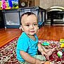 toddler, child, toy, plush_toy, carpet, wooden_floor, blue_shirt, green_pants, living_room, television, animated_show, furniture, playpen, smiling, sitting, indoors, cute, baby, floor_play, home
