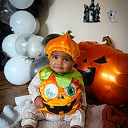 Leo joined the competition — help win amazing prizes! baby, child, pumpkin_costume, halloween, balloons, inflatable, jack_o_lantern, ghost_decorations, blanket, floor, costume, holiday, indoor, cute, sitting, expression, orange, green, black, white