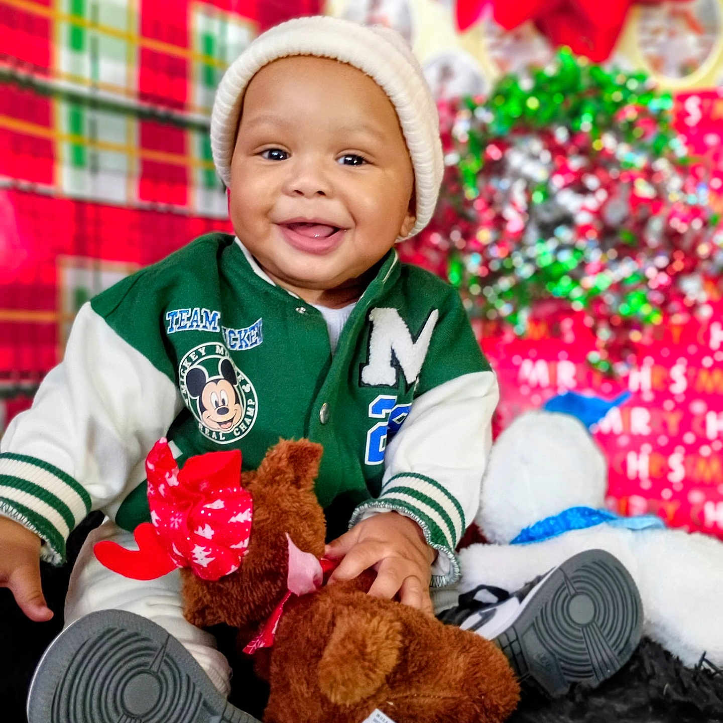 Kei'Jon joined the competition — help win amazing prizes! baby, beanie, black_rug, child, christmas, cute, decorations, festive, green_jacket, happy, holiday, indoor, person, plush_toy, portrait, red_bow, reindeer, sitting, smiling, toddler