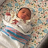 Solana is registered to the contest to win money with this photo: baby, newborn, sleeping, blanket, hat, floral_pattern, bed, crib, peaceful, infant, wrapped, child, soft, cute, indoors, resting, portrait, person, small, cozy