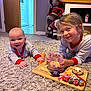 Tommy is registered to the contest to win money with this photo: baby, child, carpet, pajamas, smile, milk, glass, lollipop, pie, toy, holiday_decoration, carrot, floor, indoor, happy, person, playing, cute, family, room