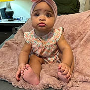 Jazleigh is registered to the contest to win money with this photo: baby, child, infant, headband, pink_bow, floral_outfit, blanket, soft_texture, sitting, cute, indoors, curious, wide_eyes, pursed_lips, foot, hand, bedroom, lamp, table, home