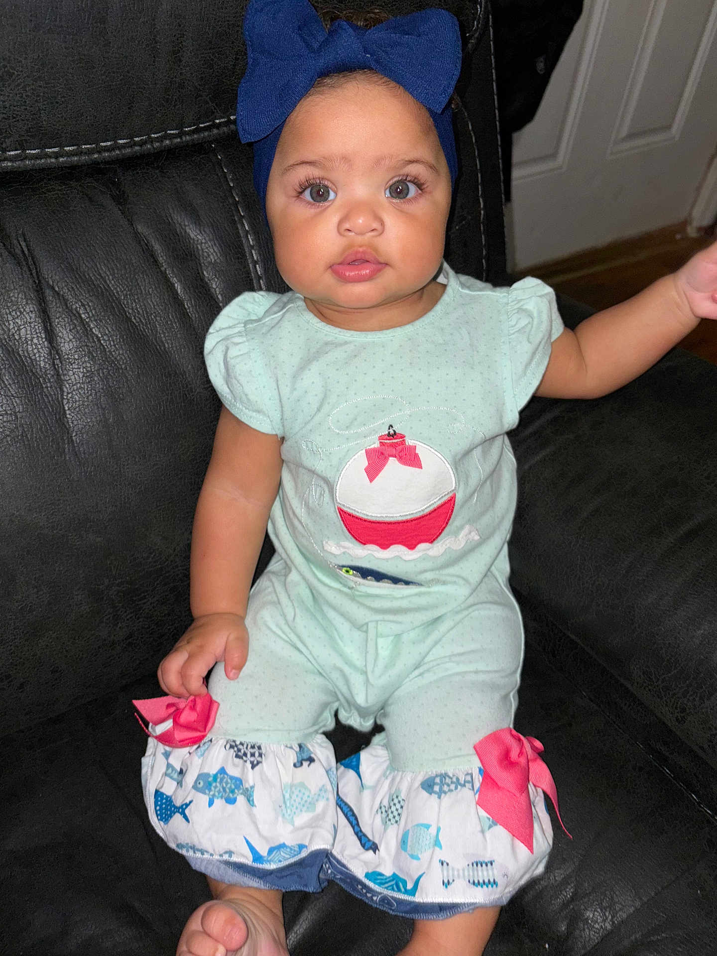 Jazleigh is registered to the contest to win money with this photo: baby, child, girl, headband, blue_bow, romper, fish_pattern, pink_bows, sitting, black_couch, indoor, curious, wide_eyes, chubby_cheeks, barefoot, clothing, portrait, cute, infant, toddler