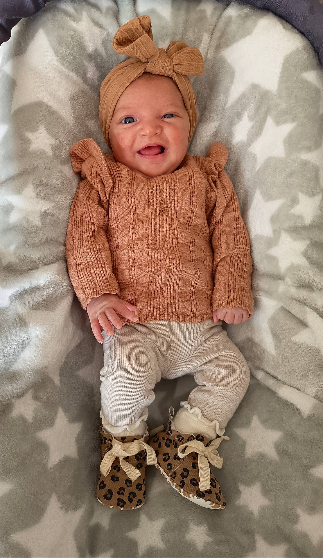 baby, baby_girl, blanket, booties, child, cozy, cute, fashion, happy, headband, indoors, infant, knitted_clothing, lying_down, newborn, portrait, smiling, soft_texture, star_pattern, warm_clothing