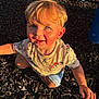 toddler, child, blonde_hair, blue_eyes, dinosaur_shirt, outdoor, playground, sunlight, happy, smiling, shorts, crouching, person, face, skin, hand, nature, daylight, casual_clothing, childhood