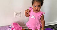 Blessin is registered to the contest to win money with this photo: carpet, chair, child, crocs, curly_hair, cute, expression, floor, home, indoor, minnie_mouse, orange_ring, person, pink_dress, play_area, purple_ring, standing, toddler, toy, wall_outlet