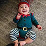 baby, infant, child, carpet, floor, costume, elf, striped_pants, red_hat, green_outfit, smiling, happy, hands, feet, indoor, cute, playful, person, apparel, portrait