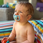 Maël a rejoint le concours — aidez-le/la à gagner de superbes lots ! baby, child, pacifier, toy, striped_cushion, blue_eyes, curious, outdoor, colorful, playful, infant, sitting, cute, soft_skin, portrait, closeup, summer, bright, warm, relaxed