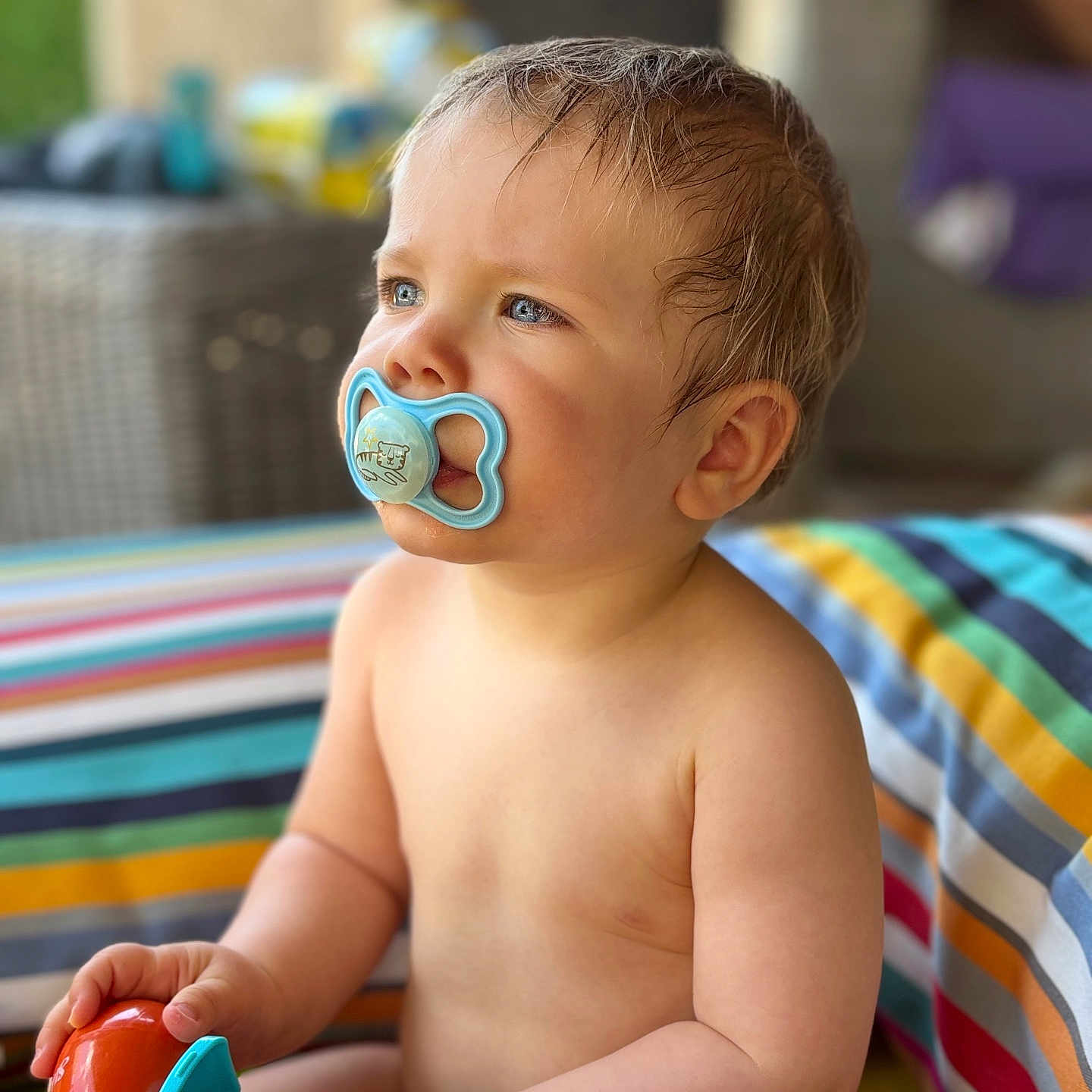 Maël a rejoint le concours — aidez-le/la à gagner de superbes lots ! baby, blue_eyes, bright, child, closeup, colorful, curious, cute, infant, outdoor, pacifier, playful, portrait, relaxed, sitting, soft_skin, striped_cushion, summer, toy, warm