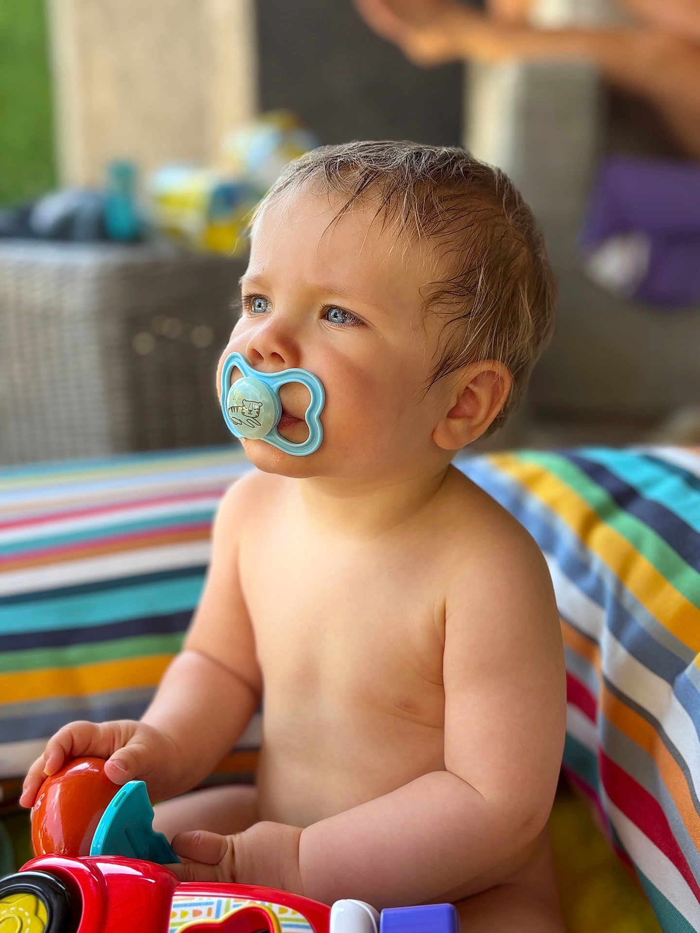 Maël a rejoint le concours — aidez-le/la à gagner de superbes lots ! baby, child, pacifier, toy, striped_cushion, blue_eyes, curious, outdoor, colorful, playful, infant, sitting, cute, soft_skin, portrait, closeup, summer, bright, warm, relaxed