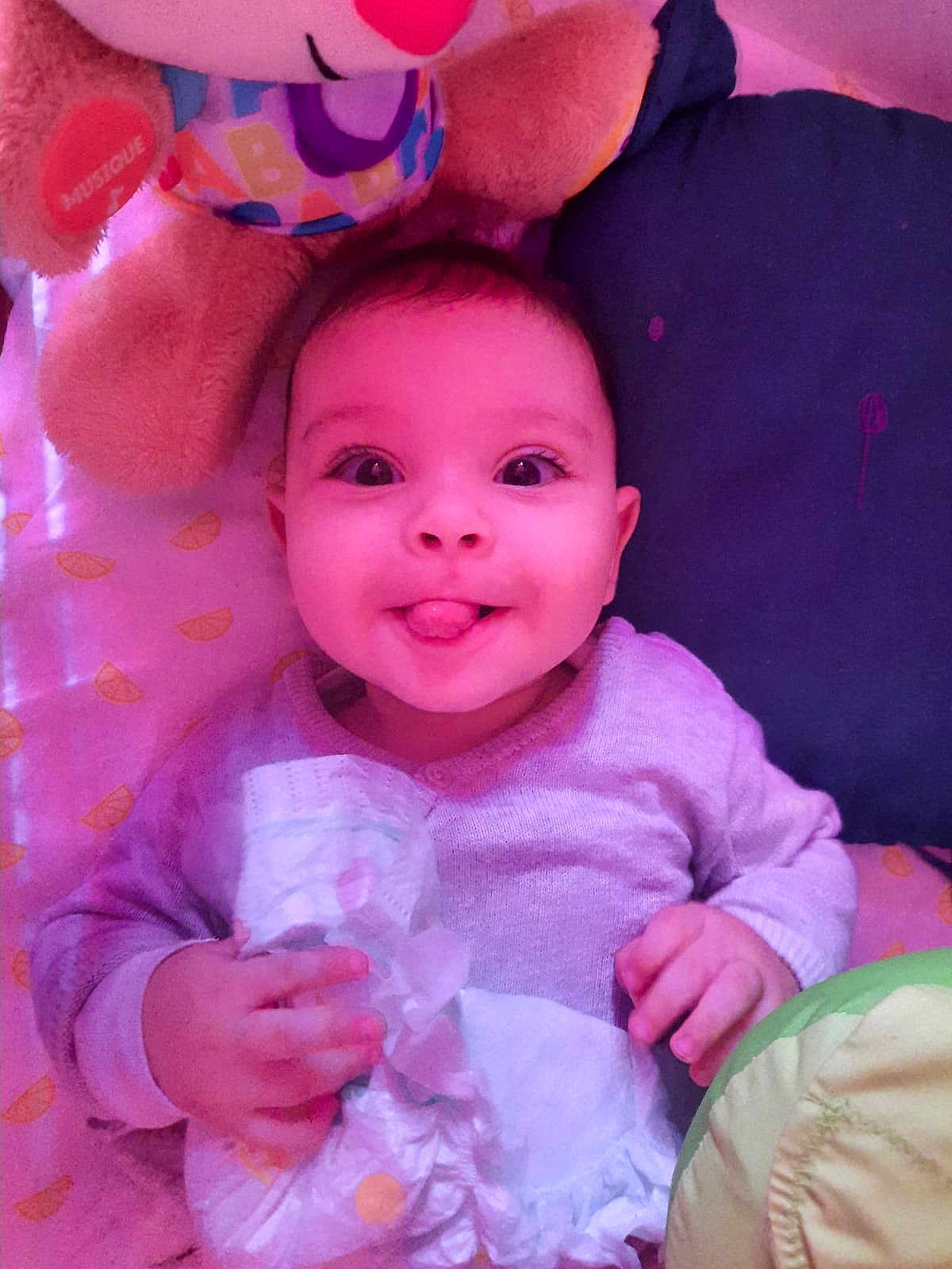 Ahmed participe au concours pour gagner de l'argent avec cette photo : baby, infant, diaper, toy, smiling, tongue_out, bed, pillow, blanket, cute, child, playful, happy, soft_toy, clothing, hand, face, indoors, lying_down, expression